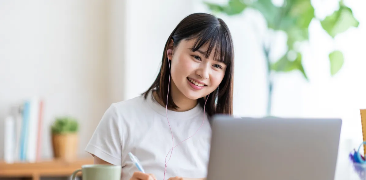 イヤホンをつけてパソコンに向かう笑顔の女性